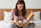 Woman smiling while unboxing natural skincare products on bed